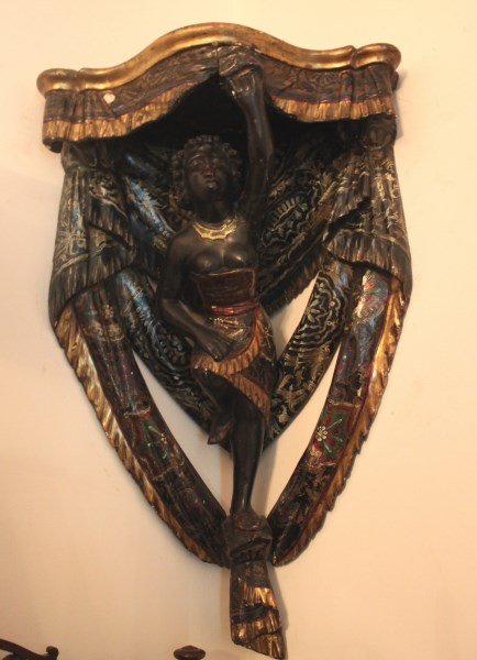 Good Italian Blackamoor Bracket,: with a shaped top supported by figure with carved drape surrounds, in tones of gilt and black