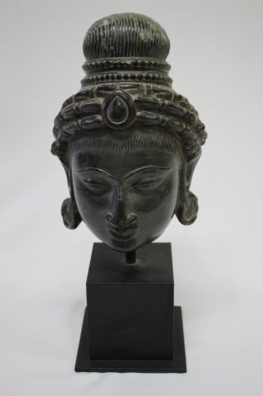Carved Black Stone Head of Deity,: possibly 14/15th Century Rajasthan Stone, with top knot, and striated hair, with carved central jewel motif, the eyes of almond form, with a beautiful serene expression, on later metal and slate stand