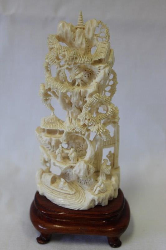 Chinese Carved Ivory Sculpture,: tusk carved as a pillar of rock, with wild pine trees growing upon it and various pavilions and figures nestled, on a wooden stand, h 13cm