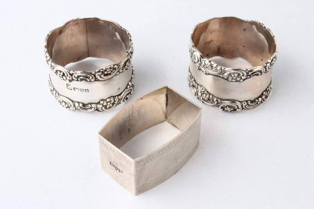 Pair and Single Chester Sterling Silver Napkin: Rings, the pair hallmarked Chester, 1903, by Latham and Morton, circular with applied foliate scroll borders; the other hallmarked Chester,1929, J.Gammage (?), almost rectangular with engine turned bo