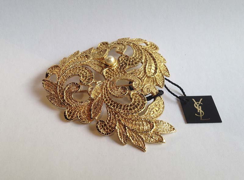 YVES-SAINT-LAURENT. Broche: Metal dorte. Motif de rinceaux, 1 perle Poincon