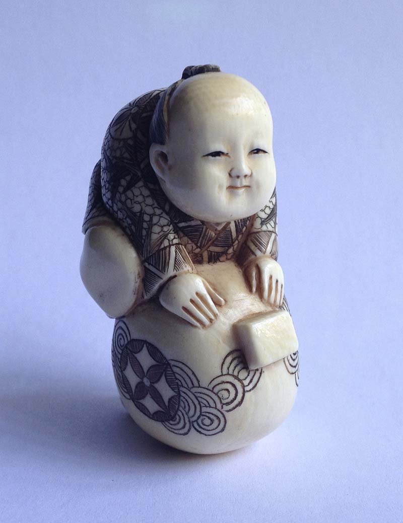 Japon, debut XXe. Netsuke Enfant sur une pierre sacree: Japon, debut XXe Netsuke Enfant sur une pierre sacree Ivoire sculpte, teinte dans les creux et signe Haut. 5,5 cm.