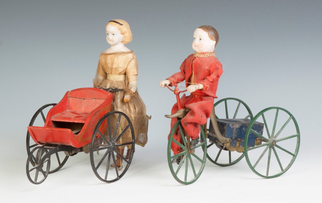 Two Clockwork Toys: Two Clockwork Toys. 19th cent. Paper mache heads. Lady w/cart, very good, Ht. 11". Boy on tricycle, spring un-wound, Ht. 10 1/2". .