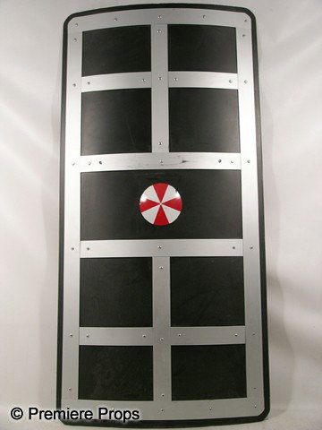 Resident Evil Afterlife Umbrella Trooper Shield Mo: Resident Evil Afterlife - Umbrella Trooper's black plastic with 'Umbrella' logo and silver metal squares on the front, silver metal handle and stand on the back, shield with a few scratches on the fro