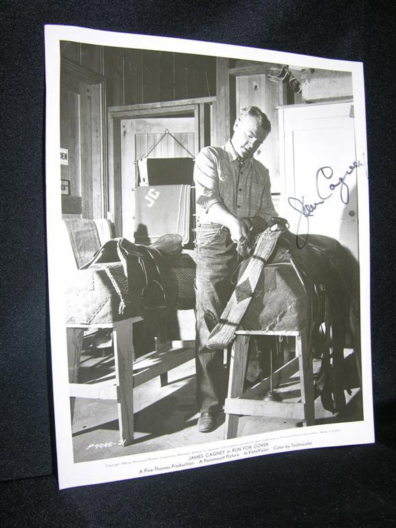 James Cagney Signed Photo: Black and white 8 x 10 vintage photo of James Cagney in the 1954 motion picture Run For Cover, signed by Cagney in black marker. The picture depicts Cagney in a shadowy pose, handling a horse saddle. 