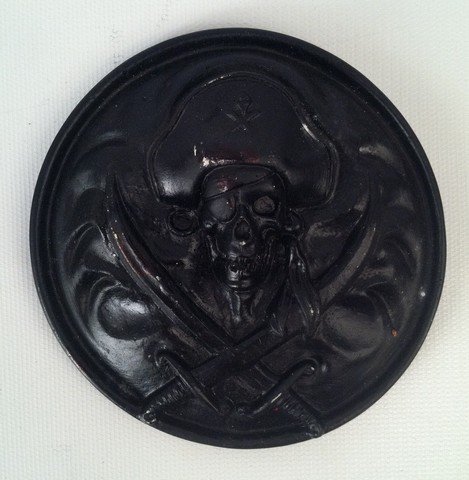 Pirates of the Caribbean Disneyland Ride Cross-Bones: An ghoulish sword and cross-bones plaque, painted coal black which hung for years on the "Pirates of the Caribbean" ride at Disneyland in California. Approx. 4.75" diameter.