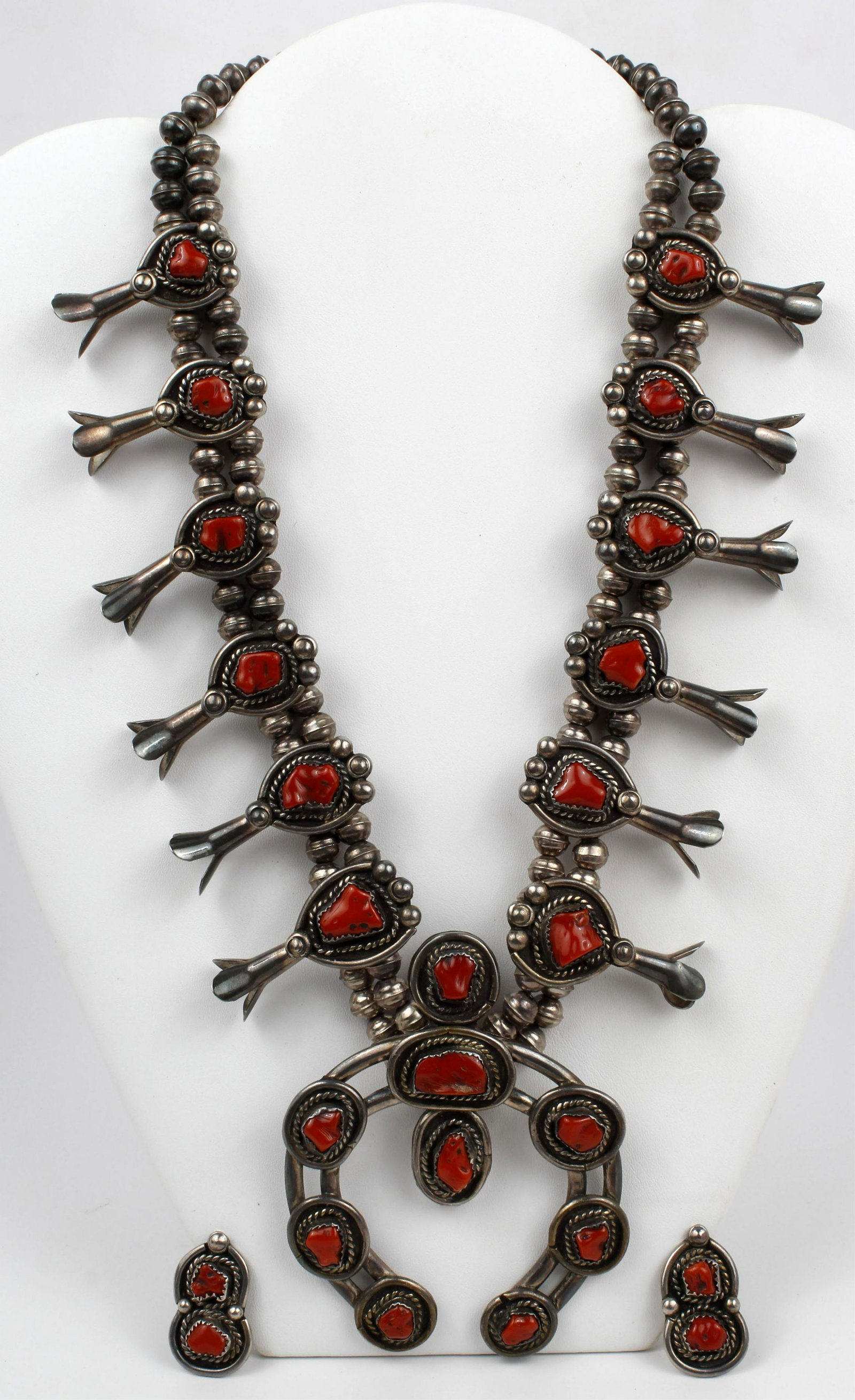 NAVAJO SILVER CORAL SQUASH BLOSSOM NECKLACE SET: Navajo silver and coral squash blossom necklace. Twelve graduated squash blossoms, each set with a coral cabochon and accented with silver beadwork and rope design applique; the central wire naja is s
