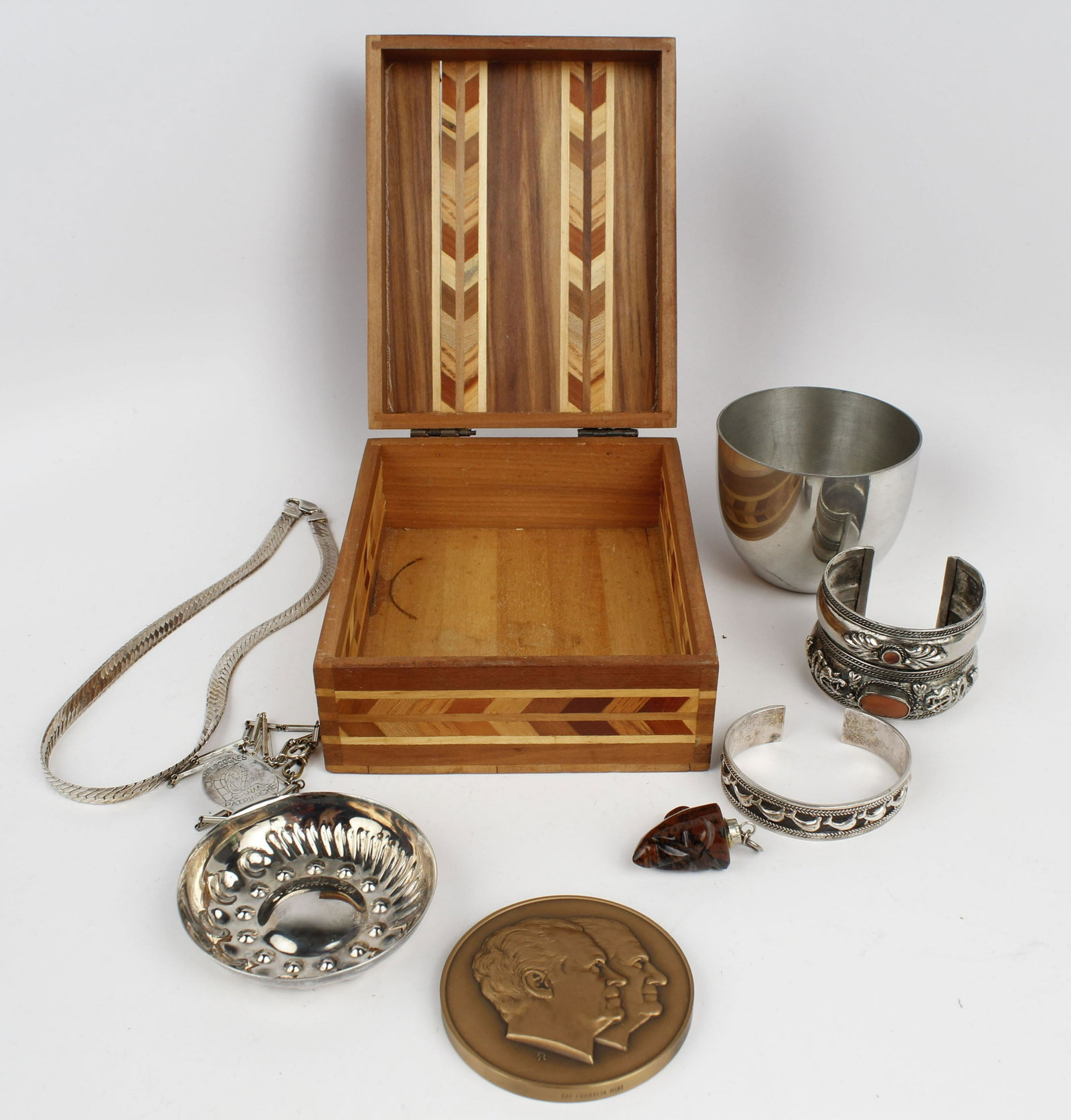 WOODEN BOX OF ASSORTED SILVER TRINKETS: Box to include: Silver clad cuff, Silver wine taster, Sterling silver dolphin cuff 28.47 grams, Sterling silver necklace 32.15 grams, Mayan head pendant, Nixon commemorative coin paperweight. Conditio