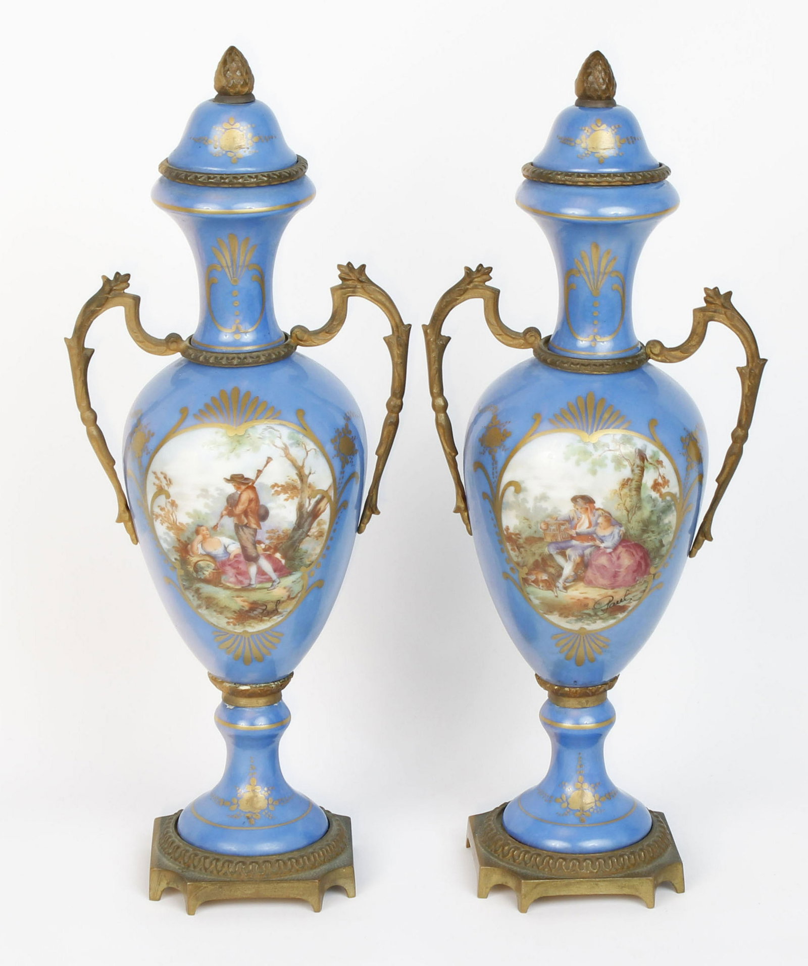19TH CENTURY HAND PAINTED FRENCH VASES: A pair of French twin handles ormolu garniture lidded urns with serves hand painted porcelain circa 1870. Pear shaped enclosing, picnic scene on indigo round and raised gild bronze 8 leg pint. SignedG