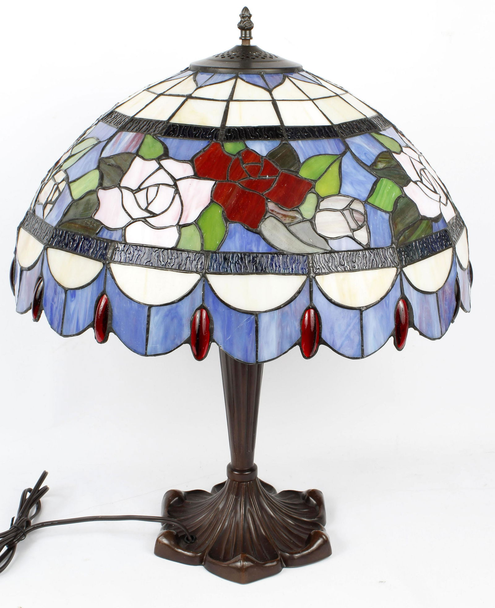 TIFFANY STYLE LAMP BRONZE STAINED GLASS JEWELS: Vintage Tiffany style lamp. Base is 25" high. Bronze finish over white metal. Shade is 20.5" diameter by 11" high. Vintage stained glass rose pattern with red oblong jewels. 2 bulbs. Condition: Very F