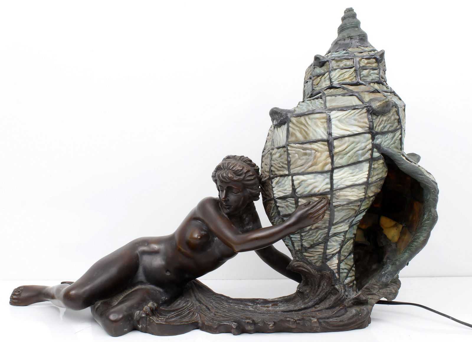 BRONZE STAINED GLASS SHELL LAMP WITH NUDE WOMAN: 115186BRONZE STAINED GLASS SHELL LAMP WITH NUDE WOMAN Figural nude maiden reclining and holding a large stained glass conch shell light. Signed Wuyh and dated 1992. Measures 15H x 21L. Light has been