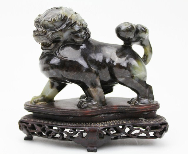 CHINESE JADE FOO DOG ATOP WOODEN BASE: CHINESE JADE FOO DOG ATOP WOODEN BASE Chinese jade foo dog. Black with gray accents intertwined throughout the piece standing upon a wooden base. The base is missing one leg but still stands perfectly