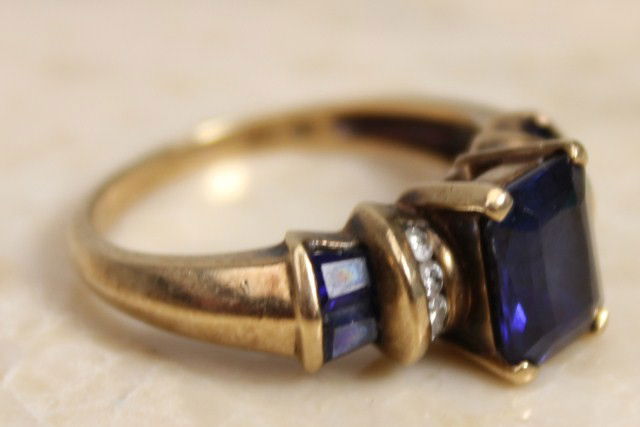 LADIES 10K GOLD RING W/ COBALT BLUE SPINEL STONE: A ladies 10K yellow gold ring with 3 cobalt blue spinel stones. Centered is an emerald cut spinel and adjacent are 8 accent diamonds. Weight: 3.8 g Size: 7.75 Condition: VGC
