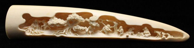 A FINELY CARVED ELEPHANT IVORY TUSK VILLAGE SCENE: A FINELY CARVED ELEPHANT IVORY TUSK VILLAGE SCENE A juvenile elephants tusk, carved with intricate precision by a craftsman. The figures are delicate and show a scene captured on the edge of a wood wi