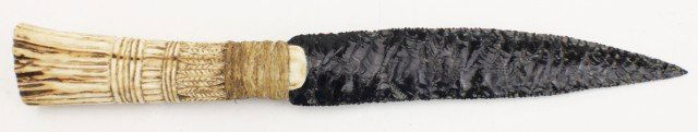 OBSIDIAN FLAKED STONE KNIFE ANTLER HANDLE: OBSIDIAN FLAKED STONE KNIFE ANTLER HANDLE Handmade obsidian blade of 7" set into a stag antler hilt and secured by rope. The handle is carved to represent a bundle of wheat at harvest time. Size: 12 x
