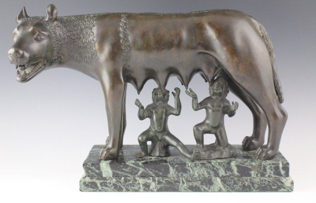 AFTER CAPITOLINE WOLF BRONZE STATUE: AFTER CAPITOLINE WOLF BRONZE STATUE A bronze statue after the Capitoline Wolf featuring the founders of Rome, Remus and Romulus being suckled by the legendary She-Wolf. Seated on marble plinth. , Size
