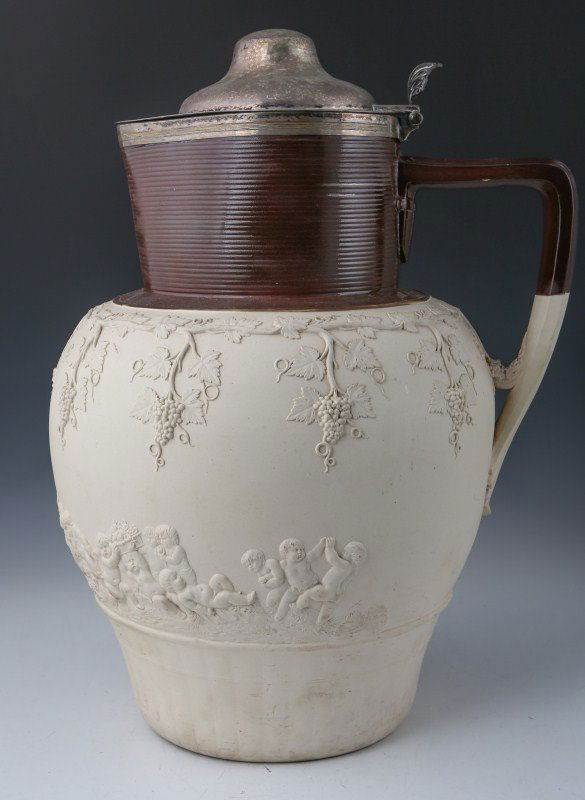 A HUGE CONTINENTAL EARTHENWARE WINE PITCHER: A HUGE CONTINENTAL EARTHENWARE WINE PITCHER Decorated with vine and grapes. Cherubs below. Brown glazed rim. White metal jug lid. This monumental piece would grace any farmhouse kitchen. Size: Almost