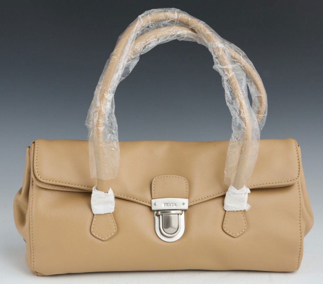 PRADA CREAM COLORED LEATHER HAND BAG: PRADA CREAM COLORED LEATHER HAND BAG Prada rectangular bag with two hard handles, Prada plaque on the side and front clasp, fully lined, includes card of authenticity. Bag is inside white cloth Prada