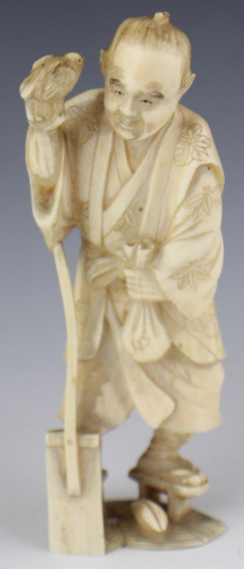JAPANESE IVORY CARVING FARMER SIGNED: JAPANESE IVORY CARVING FARMER SIGNED A Japanese carved ivory figure of a standing farmer, right arm propped on his hoe, supporting a bird perched on his closed fist. His left hand clutches a closed sa