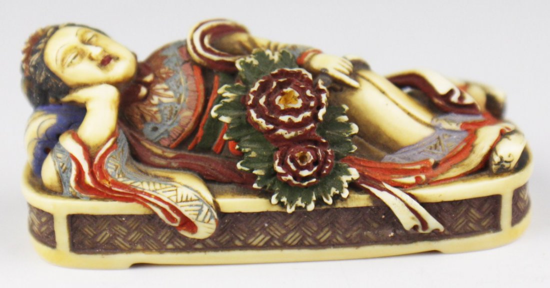 CARVED IVORY POLYCHROME RECLINING NETSUKE: CARVED IVORY POLYCHROME RECLINING NETSUKE A very intricately carved ivory netsuke. Features a female reclining on a rectangular plinth, holding a pair of flowers in her left hand, while her right prop