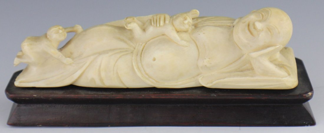 CARVED IVORY RECUMBENT BUDDHA: CARVED IVORY RECUMBENT BUDDHA A carved ivory recumbent buddha figure, complete with two playful children and a happy facial expression. Set on wooden base. Size: 6 x 1 1/3" **Please be advised: Intern