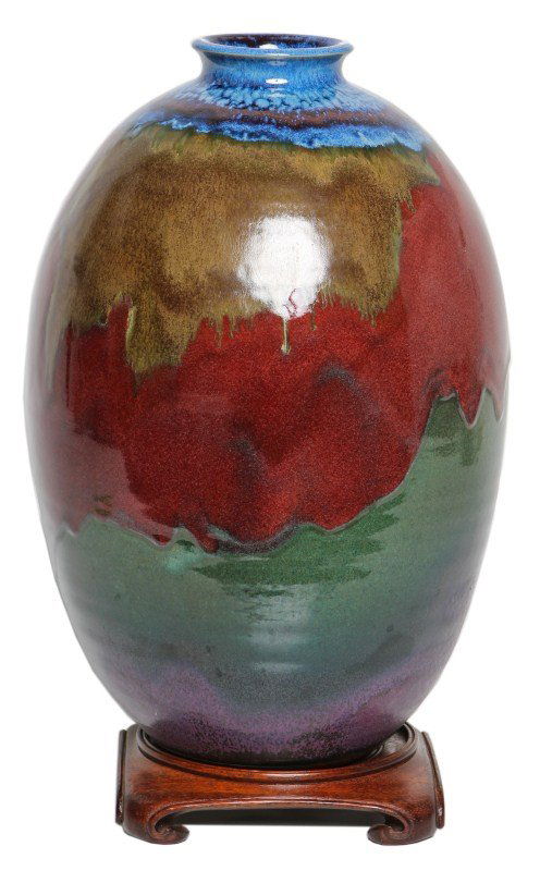 LARGE OVOID EARTHENWARE ART VASE WITH STAND: LARGE OVOID EARTHENWARE ART VASE WITH STAND Large ovoid shaped ceramic vase with multicolor glaze design using muted green, yellow, blue, and red. Includes wood base. Size: 19" on stand