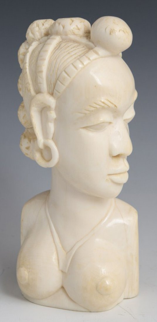 CARVED AFRICAN IVORY FEMALE BUST: CARVED AFRICAN IVORY FEMALE BUST African female bust carved of ivory. Features a topless female, adorned with necklace, earrings and hair sorted into seven buns. Her stern expression is directed towar