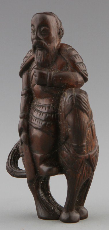 JAPANESE CARVE WOODEN NETSUKE FIGURE: JAPANESE CARVE WOODEN NETSUKE FIGURE Japanese carved wooden netsuke of scholarly figure riding horse. Figure resembles a scholar, and is carrying a sword and grasping his beard. Size: 2.75 x 1.25 x .7