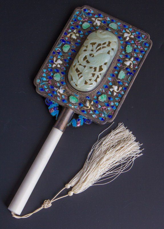CHINESE ENAMELED SILVER & JADE MIRROR IVORY HANDLE: CHINESE ENAMELED SILVER & JADE MIRROR IVORY HANDLE Chinese mirror. Sterling back with enamel and jade accents. Large jade floral carving set in center. Ivory handle with tassel. Late 19th century. Siz