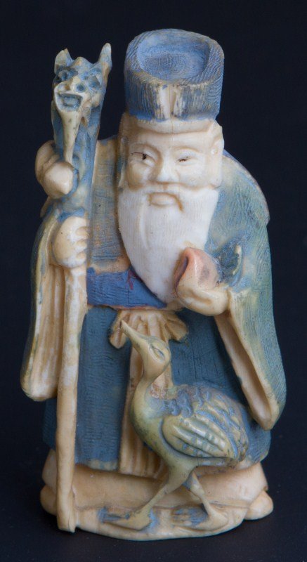 IVORY POLYCHROME NETSUKE SHOU-LOU: IVORY POLYCHROME NETSUKE SHOU-LOU Carved ivory polychrome netsuke featuring Taoist god of life and luck, shown carrying a dragon staff, pumpkin gourd, peach of immortality and with a crane. Signed on 