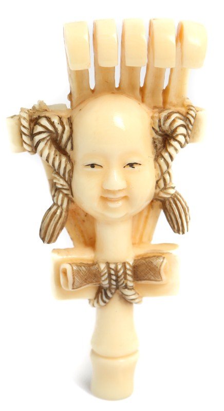 JAPANESE CARVED IVORY NETSUKE RAKE SIGNED: JAPANESE CARVED IVORY NETSUKE RAKE SIGNED A Japanese carved ivory netsuke in the shape of a rake with a face. Two of the tines are missing. Signed. Size: 3.25"