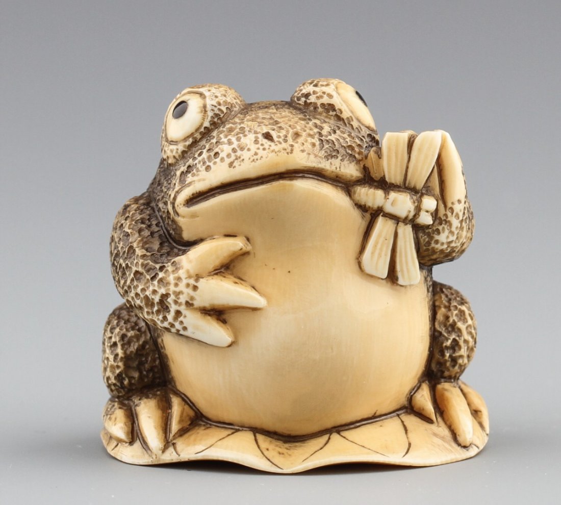 JAPANESE CARVED IVORY NETSUKE FROG W/ DRAGONFLY: JAPANESE CARVED IVORY NETSUKE FROG W/ DRAGONFLY Japanese carved ivory netsuke figure of a frog on a lily pad eating a dragonfly. Monochrome. Signed, Tomomasa. Size: 1.5 x 1.5 x 1.25" Weight: 46g