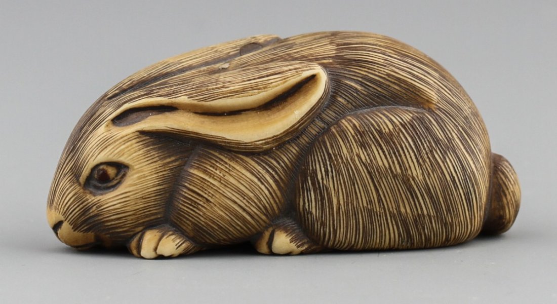 JAPANESE CARVED IVORY NETSUKE HARE BAISHO: JAPANESE CARVED IVORY NETSUKE HARE BAISHO Early 20th century Japanese carved ivory netsuke of resting hare; Some patina with monochromed detail, signed Baisho. Size: 2"l Weight: 27g