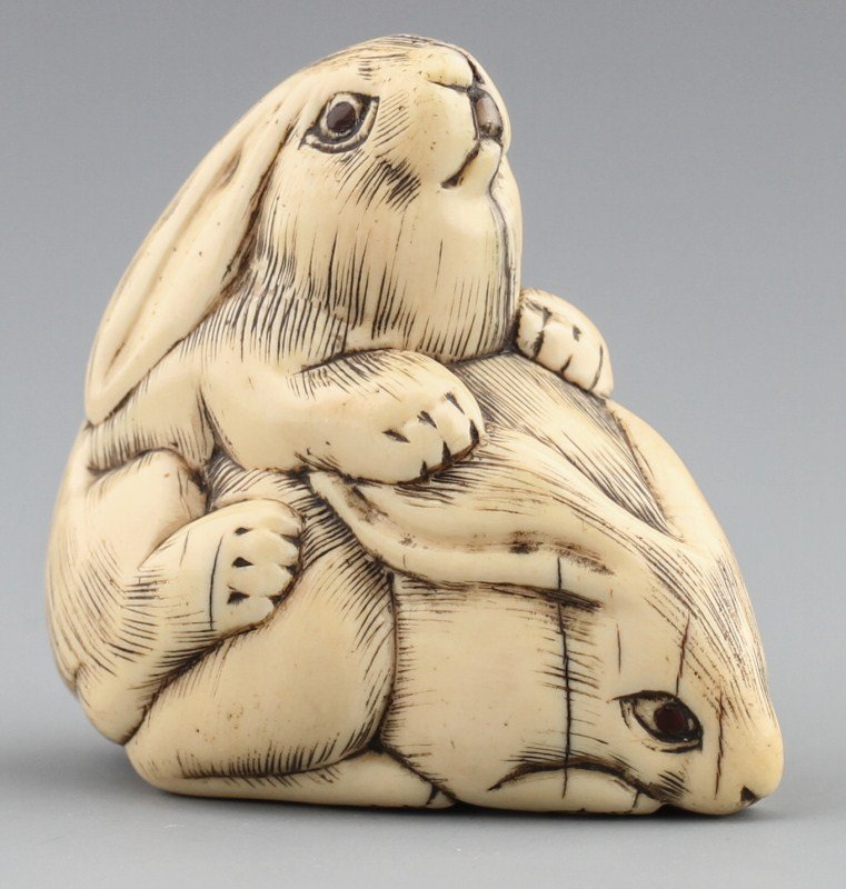 JAPANESE CARVED IVORY NETSUKE TWO HARES: JAPANESE CARVED IVORY NETSUKE TWO HARES Japanese carved ivory netsuke of two rabbits mating. Monochromed, Signed. Size: 1.75 x 2 x 1" Weight: 38g