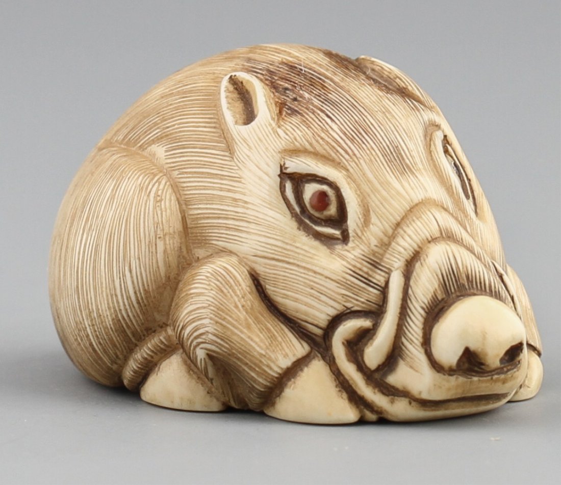 JAPANESE CARVED IVORY NETSUKE WARTHOG BAISHO: JAPANESE CARVED IVORY NETSUKE WARTHOG BAISHO Early 20th century Japanese ivory carved netsuke of warthog with monochromed detail and red cabochon eyes, signed Baisho. Size: 1 5/8"l Weight: 26g
