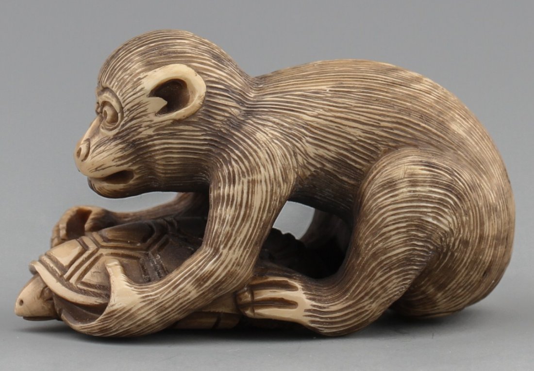 JAPANESE CARVED IVORY NETSUKE MONKEY AND TURTLE: JAPANESE CARVED IVORY NETSUKE MONKEY AND TURTLE Japanese carved ivory netsuke figure of money catching a turtle with monochromed detail, Signed. Size: 1 7/8"l Weight: 25g