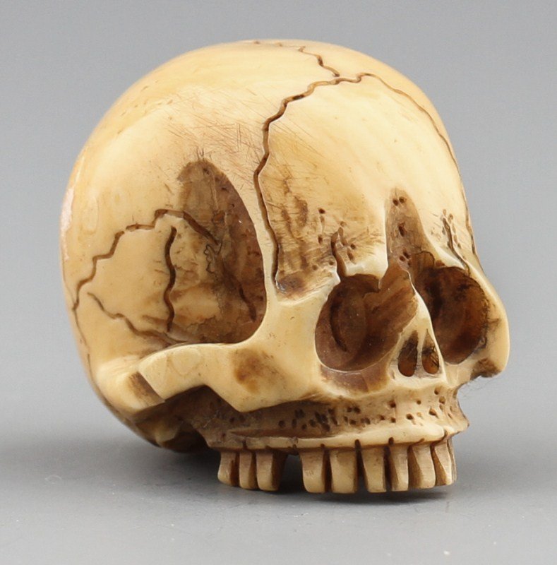 JAPANESE CARVED IVORY NETSUKE SKULL: JAPANESE CARVED IVORY NETSUKE SKULL Japanese carved ivory netsuke figure of a skull. Signed. Size: 1 x 1 x .75" Weight: 14.3g