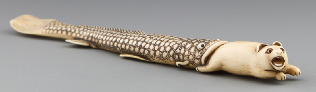JAPANESE CARVED IVORY SASHI NETSUKE OF CATFISH: JAPANESE CARVED IVORY SASHI NETSUKE OF CATFISH Japanese carved ivory sashi netsuke of catfish swallowing a small mammal, Signed Baisho. Size: 8"l Weight: 60g