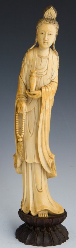 CARVED ELEPHANT IVORY CHINESE GUANYIN FIGURE: CARVED ELEPHANT IVORY CHINESE GUANYIN FIGURE Carved elephant ivory figure of Guanyin on wood base, C.19th century. Even age patina. She holds a vase and a string of beads with tassel. Size: 14"