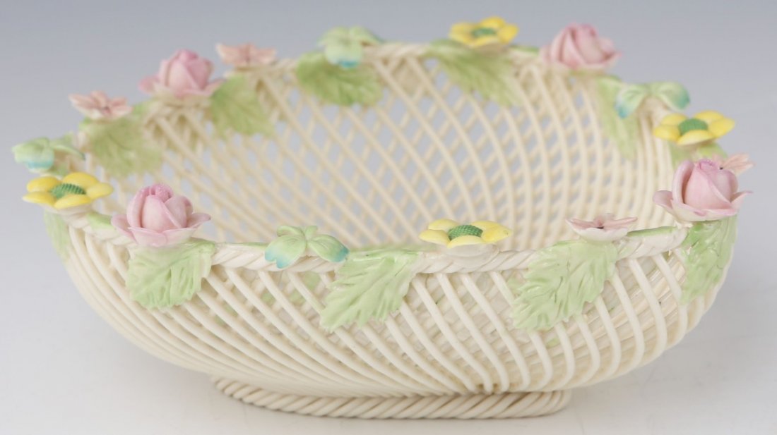 BELLEEK IRELAND WOVEN PORCELAIN BASKET: BELLEEK IRELAND WOVEN PORCELAIN BASKET A woven porcelain basket, rim decorated with porcelain flowers and leaves that drape over its lip. The basket forms a heart, and consists of a variety of pinks,