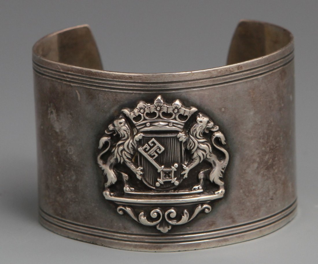 SILVER PLATED CUFF BRACELET CONVERTED NAPKIN RING: SILVER PLATED CUFF BRACELET CONVERTED NAPKIN RING Hallmarked, converted cuff bracelet napkin ring, displays large coat of arms depicting a pair of rampant lions and skeleton key in the center. Incompl