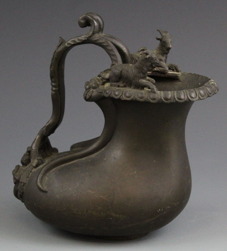 NEO-CLASSICAL BRONZE ASKOS WINE PITCHER: NEO-CLASSICAL BRONZE ASKOS WINE PITCHER Neo-Classical Bronze Askos Wine Pitcher, likely Continental, 19th C. Decorated with goats, acanthus leaves, and Eros. Nice patina. Size: 7"