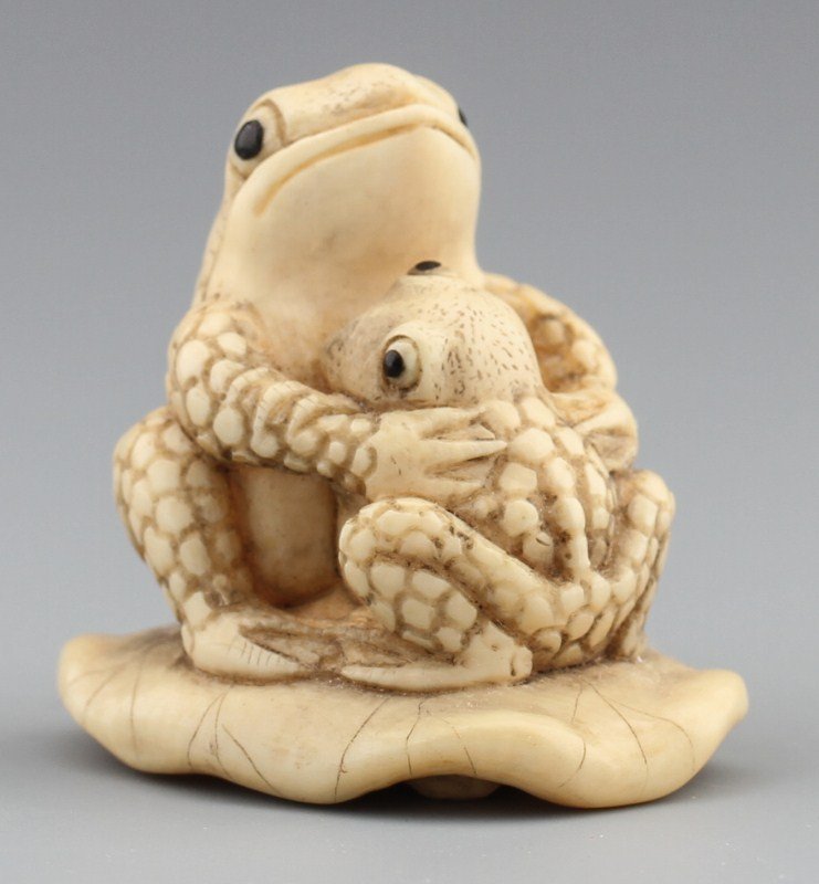 JAPANESE CARVED IVORY NETSUKE TWO TOADS: JAPANESE CARVED IVORY NETSUKE TWO TOADS Japanese carved ivory netsuke figure of two toads embracing on lily pad. Signed, Tomoichi. Size: 1.5 x 1.5 x 1.25" Weight: 29g