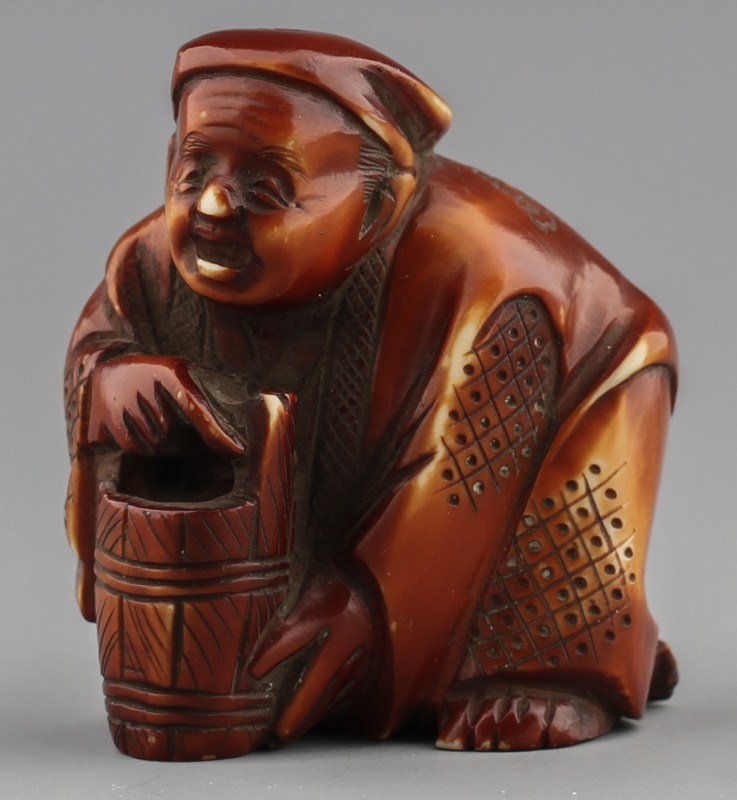 JAPANESE CARVED IVORY NETSUKE MAN W/ WATER BARREL: JAPANESE CARVED IVORY NETSUKE MAN W/ WATER BARREL Japanese carved ivory netsuke figure of man with water barrel. Stained. Signed. Size: 2 x 1.75 x 0.75" Weight: 37g