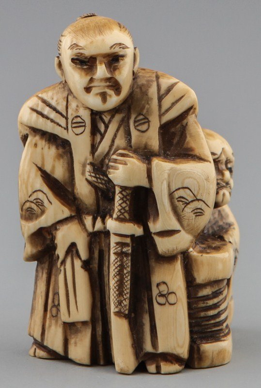 JAPANESE CARVED IVORY NETSUKE THE PROTECTOR: JAPANESE CARVED IVORY NETSUKE THE PROTECTOR Japanese carved ivory netsuke of man preparing to draw his sword to protect his father. Son has a face of disgust and anger while father is cowering behind 