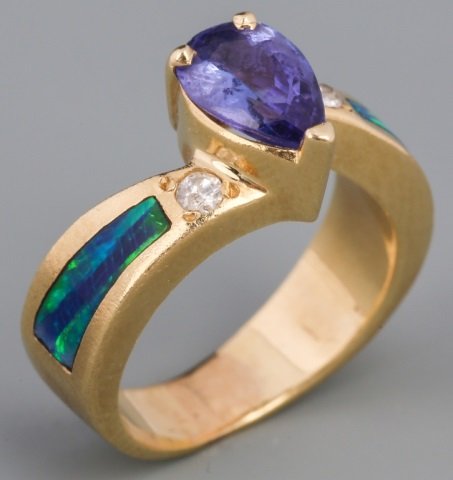 14K TANZANITE DIAMOND AND BLACK OPAL RING: 14K TANZANITE DIAMOND AND BLACK OPAL RING 14k yellow gold ring featuring 1ct pear shaped tanzanite with one diamond on each side, weighing .05 ct. Black opal inlay accents the shank. . Weight: 6.2 g S