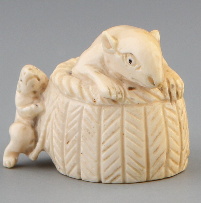 JAPANESE CARVED IVORY NETSUKE RAT IN BASKET: JAPANESE CARVED IVORY NETSUKE RAT IN BASKET Japanese carved ivory netsuke figure of a rat peeking out of a basket with baby rat on outside. Signed. Weight: 20g Size: 1 x 1.25"