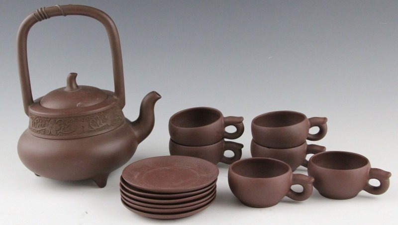 CHINESE YIXING ZISHA TEAPOT W/ 6 CUPS & SAUCERS: CHINESE YIXING ZISHA TEAPOT W/ 6 CUPS & SAUCERS Chinese Yixing Zisha teapot with floral motif and bamboo handle, stamped on bottom "Zhou Guizhen", 9 x 6.5". With a set of 6 Yiking cups with matching s