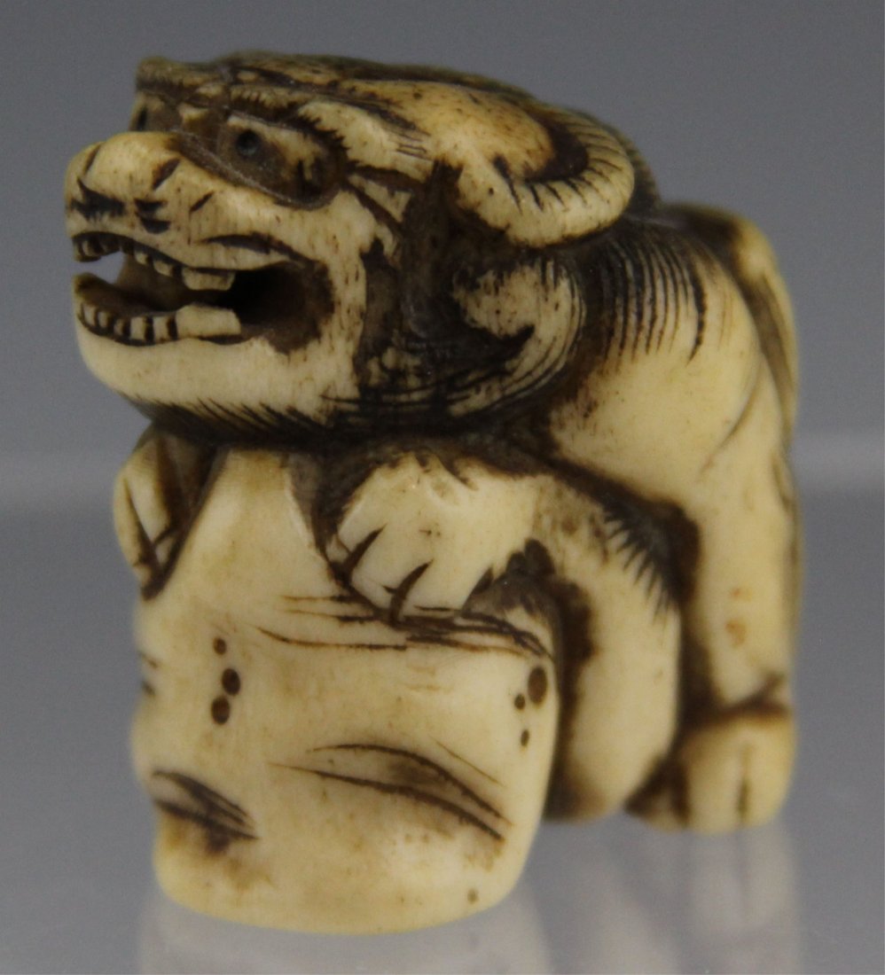 JAPANESE CARVED STAG ANTLER NETSUKE SHISHI: JAPANESE CARVED STAG ANTLER NETSUKE SHISHI Japanese carved stag antler netsuke of seated Shishi dog with large ball, 19th C.; smaller loose ball in mouth, unsigned. Weight: 19.6g Size: 1.25 x 1.25"