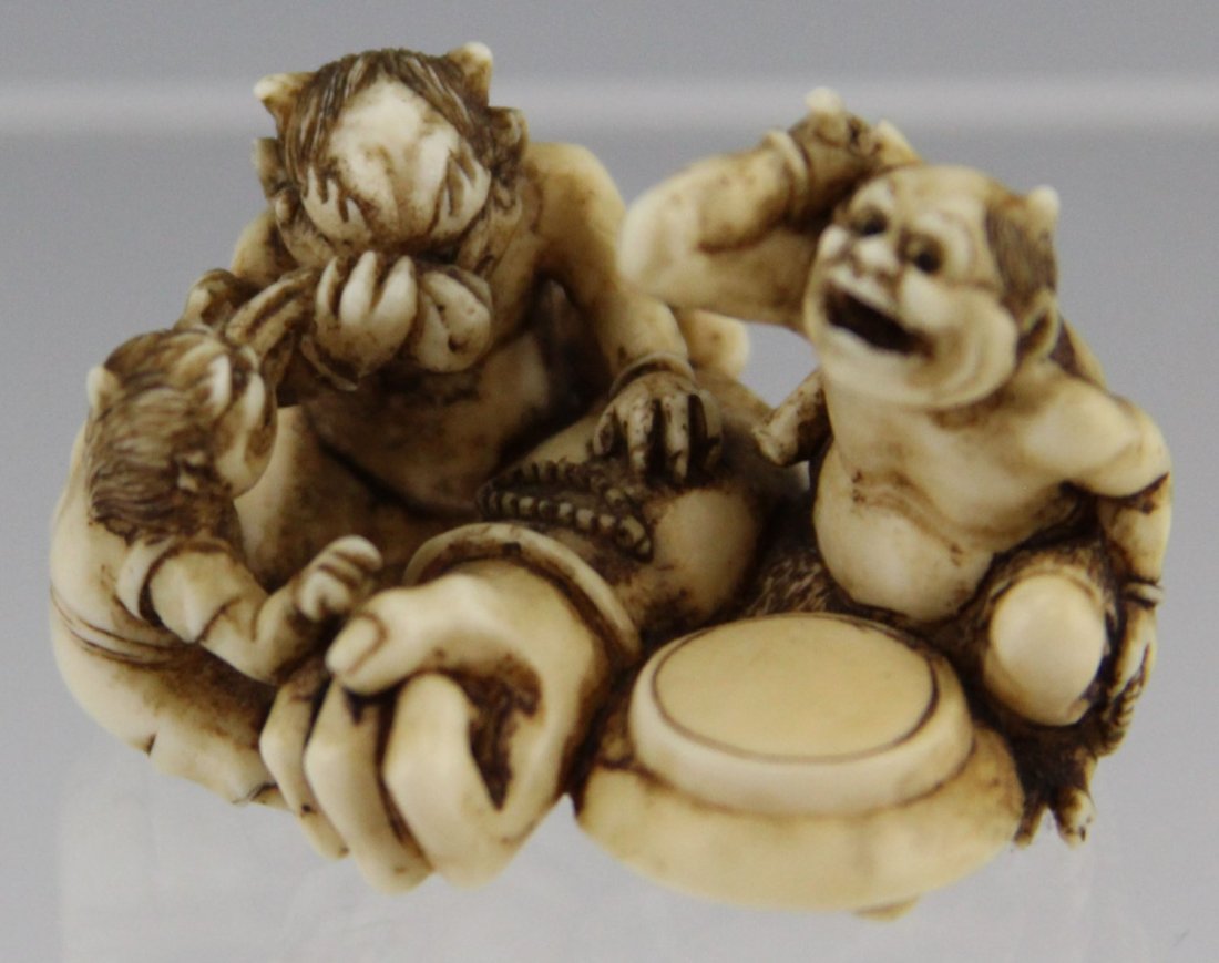 JAPANESE CARVED IVORY NETSUKE ONI WITH HAND: JAPANESE CARVED IVORY NETSUKE ONI WITH HAND Japanese carved ivory netsuke of three Oni surrounding a severed hand, late 19th/ early 20th C., stained to enhance details. Signed on underside. Weight: 11